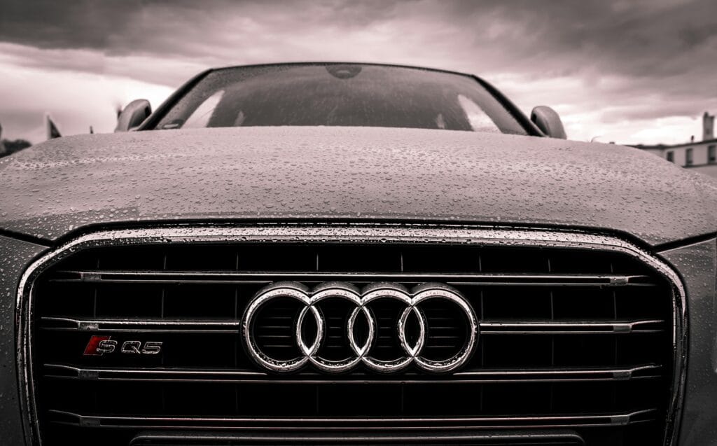 Close-up of a rain-covered Audi car grille showcasing luxury and elegance under cloudy skies.